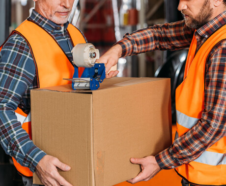 cropped view of male workers in helmets packing cardboard box with scotch tape