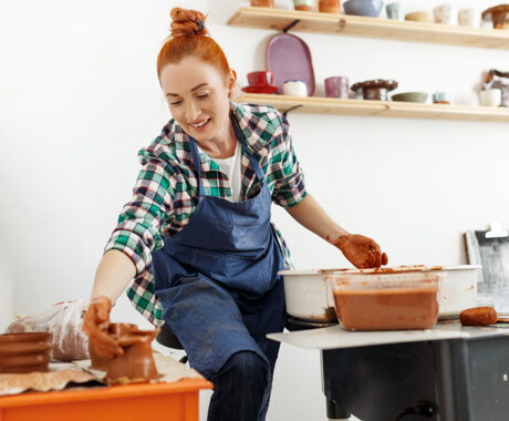 Cheerful female sculptor while she making clay pot on pottery wheel. Idea of small business and entrepreneurship. Home hobby, entertainment and leisure. Art studio.