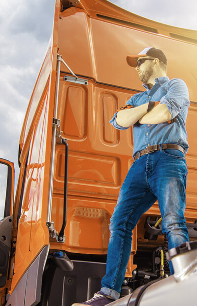 Proud Caucasian Trucker in His 30s and His Brand New Semi Truck Tractor. Truck Driver Staying on Top of the Vehicle Rear End. Heavy Duty Transportation Industry.