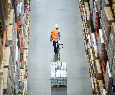 Loader pulling forklift while moving along aisle between shelves with boxes