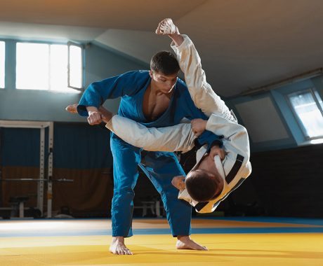 Two young judo caucasian fighters in white and blue kimono with black belts training martial arts in the gym with expression, in action, motion. Practicing fighting skills. Overcoming, reaching target.