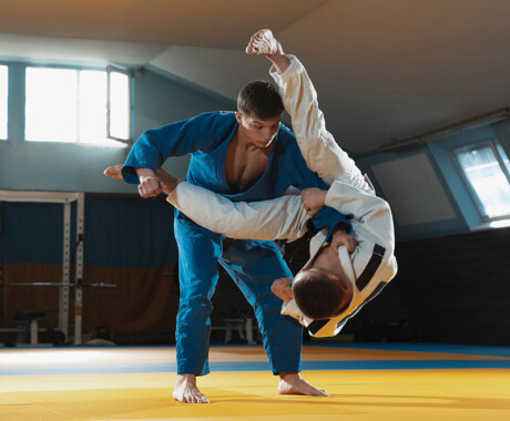 Two young judo caucasian fighters in white and blue kimono with black belts training martial arts in the gym with expression, in action, motion. Practicing fighting skills. Overcoming, reaching target.